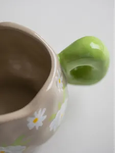 Detail of hand-painted daisy pattern and green donut handle on vintage ceramic coffee mug