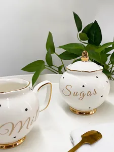 Detail of white ceramic sugar bowl and milk pitcher with gold rim and black polka dots