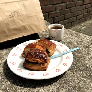 Dettaglio di piatto in ceramica con cuore, pasticcini e forchetta blu in ambiente soleggiato
