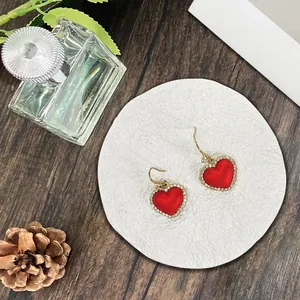 Detalle de pendientes de corazón rojo con cristales sobre posavasos y fondo de madera