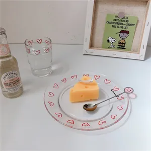 Dettaglio di un piatto e una tazza in vetro con motivi a cuore rossi dipinti a mano