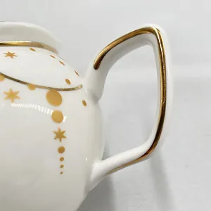 Close-up of white ceramic sugar bowl with gold star patterns and geometric handle