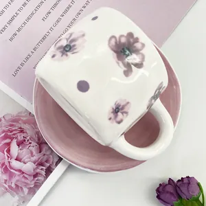 Macro view of ceramic coffee cup with hand-painted purple flowers and pink saucer