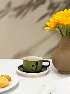 Detail of olive green ceramic coffee cup with black tulip pattern and two-tone saucer