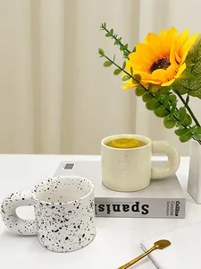 Detail of chunky ceramic mug with ink splatter pattern and large handle in a cozy setting