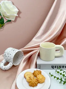 Close-up of Nordic splash ink and cream ceramic mugs with chunky rounded handles on silk