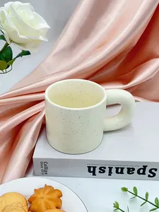 Detail of a cream ceramic mug with black ink splatters and a thick round ergonomic handle