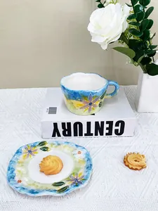 Détail d'un ensemble tasse et soucoupe en céramique peinte à la main sur nappe blanche