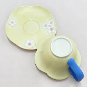 Top view of a ceramic coffee cup and saucer set with 3D floral details and a blue handle