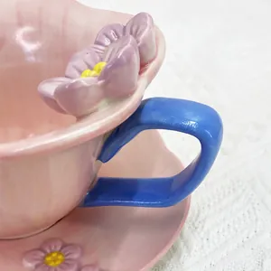 Close-up of pink ceramic coffee cup with blue handle and 3D purple flower relief detail