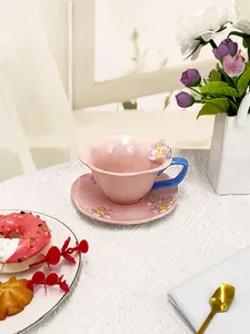Detailed view of handmade 3D floral ceramic coffee cup with blue handle on pink saucer