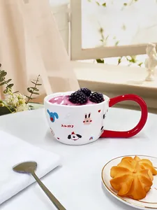 Detalle de una taza de cerámica blanca con asa roja grande y dibujos animados de animales