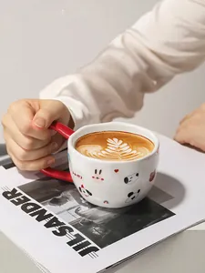Primer plano de taza de cerámica con asa roja, arte latte y dibujos de animales