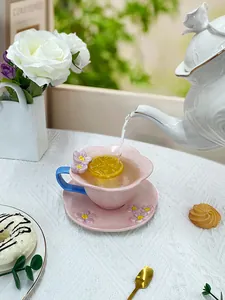 Detail of pink petal-shaped ceramic coffee cup with blue handle and 3D floral accents