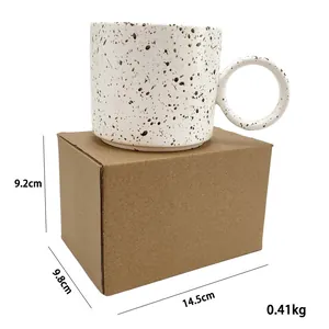Handmade ceramic coffee mug with black ink splatters and circular handle in a gift box