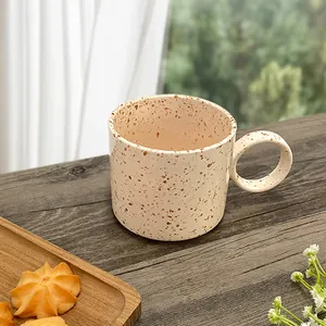 Close-up of handmade ceramic coffee mug with brown ink splash on dark wood table