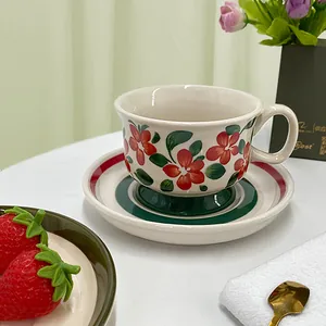 Hand-painted ceramic coffee cup and saucer set with red floral and green leaf patterns
