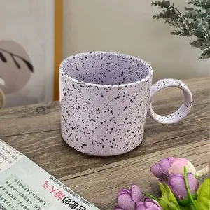 Close-up of lilac ceramic coffee mug with black ink splatters and large ring handle