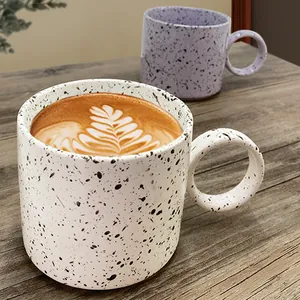 Minimalist splatter paint ceramic coffee mug with large circular handle on wooden table