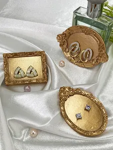 Three vintage gold-plated earrings sets displayed in ornate frames on white silk fabric