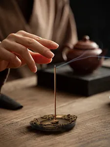 Detail of bronze incense burner with floral relief and smoke on a wooden table