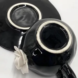 Detail of black glazed ceramic coffee cup with 3D white rose flower and matching saucer