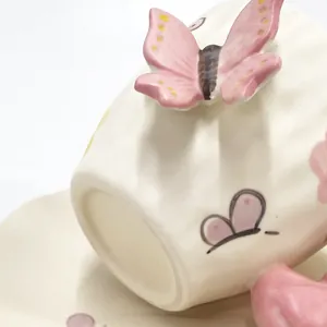 Dettaglio di tazza in ceramica crema con manico a farfalla 3D rosa e piattino coordinato