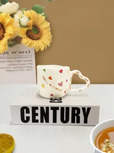 Detail van een crème keramische mok met een hartvormig handvat en handgeschilderde hartjes
