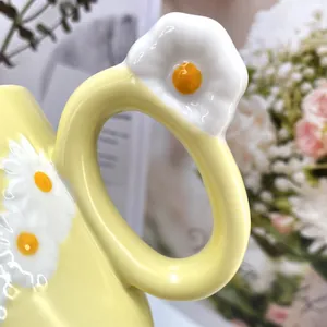 Detail of yellow ceramic mug handle with handmade 3D white daisy and glossy glazed finish