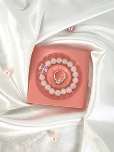 Close-up of beaded bracelet and silver diamond ring on pink resin display tray