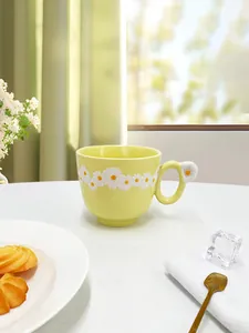 Close-up of yellow ceramic coffee mug with white daisy relief and floral handle rest