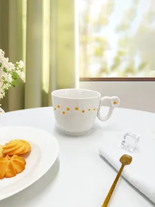 Detail of white ceramic mug featuring embossed daisy flowers and floral handle accent