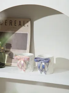 Dettaglio di tazze in ceramica bianca con manici a fiocco 3D rosa e viola cangianti