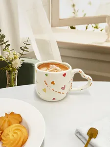 Detail van keramische mok met hartvormig handvat, getekende patronen en latte art