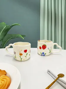 Detail van keramische mokken met handgeschilderde bloemmotieven en hartvormige handvaten