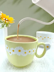 Dynamic pouring of coffee into a light green ceramic daisy mug with floral handle