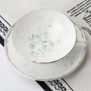 Vista dall'alto di tazza e piattino in ceramica floreale con bordo dorato su tovaglia in lino
