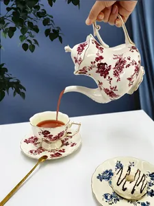 Versamento del tè da una teiera vintage in ceramica con rose rosse e bordi dorati eleganti