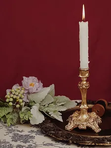 Detail of baroque gold candle holder with intricate relief patterns and lit white candle