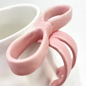 Close-up of a white ceramic mug featuring a 3D pink bow handle with delicate texture