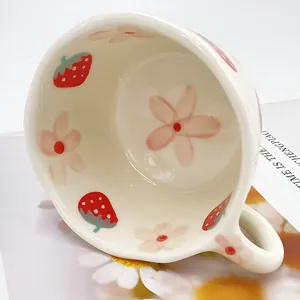 Primer plano de taza de cerámica con fresas rojas pintadas a mano y pequeñas flores rosas