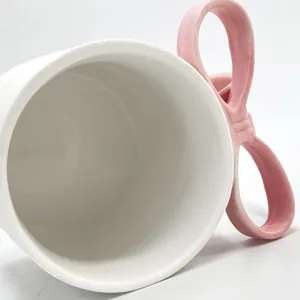 Close-up of white ceramic mug with cute 3D pink bow handle and glossy glazed finish