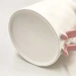 Macro detail of creamy white ceramic mug with cute 3D pink handles and smooth matte finish