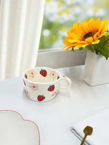 Primer plano de una taza de cerámica artesanal con fresas junto a una ventana