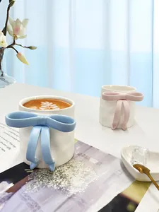 Detail of 3D ceramic mugs featuring oversized bow-shaped handles and creamy white finish