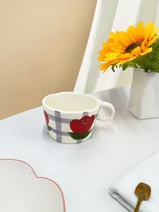 Detalle de una taza de cerámica con tulipanes y fondo de cuadros morados