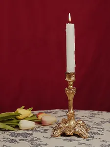 Baroque gold candlestick with relief patterns and burning white candle on velvet background