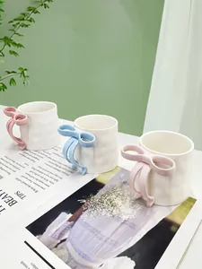Detail of 3D bow handle and wavy textured ceramic coffee mug set in a cozy home setting