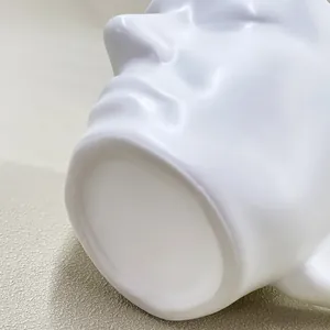 Detail view of the flat circular base and matte ceramic texture of the face-shaped coffee cup