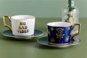 Dettaglio di tazze da caffè in ceramica con motivi Namaste dorati e manici geometrici